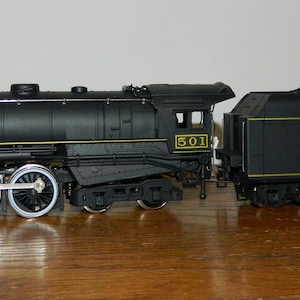 May include: A black model steam locomotive with silver wheels and yellow trim. The number 501 is printed on the cab. The tender is attached and features the text Toronto Hamilton & Buffalo Ry in yellow lettering with a load of black coal on top.