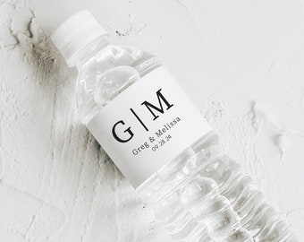 May include: A clear plastic water bottle with a white label featuring the initials "G|M", the names "Greg & Melissa", and the date "09.28.24". A matching rectangular card with the same design is also present.
