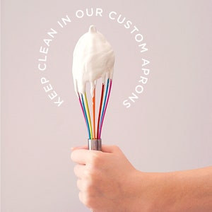 May include: A hand holding a rainbow-colored whisk with white whipped cream on the end. The text "Keep clean in our custom aprons" is written in a circle around the whisk.