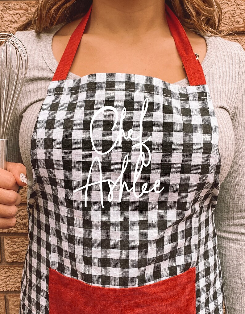 May include: Black and white checkered apron with red straps and a red pocket. The apron has the text "Chef Ashlee" written in white cursive.