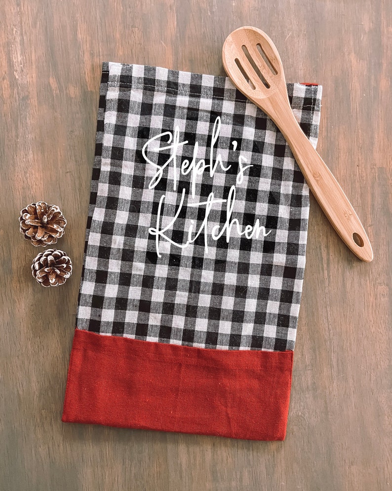 May include: Black and white checkered kitchen towel with a red border. The towel has the text "Steph's Kitchen" written in white cursive.