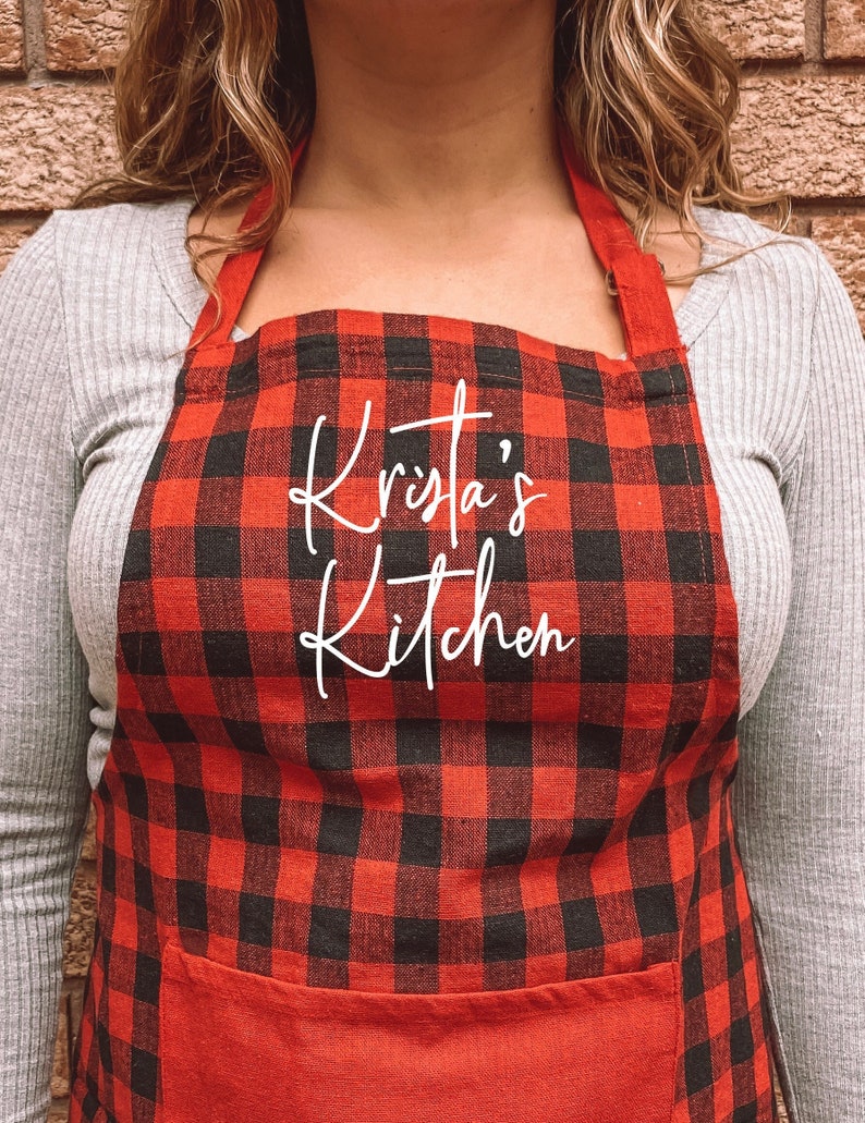 May include: Red and black buffalo plaid apron with a white embroidered pocket that says "Krista's Kitchen".