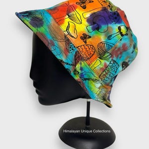 May include: A colourful bucket hat with a tie-dye pattern and black mushroom and butterfly illustrations. The hat is on a black mannequin head.