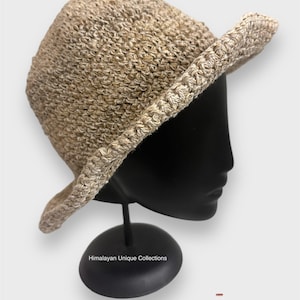 May include: A beige crocheted sun hat with a wide brim. The hat is displayed on a black mannequin head. The text "Himalayan Unique Collections" is visible on the base of the mannequin.