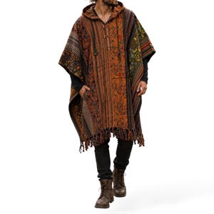 May include: A hooded poncho featuring a patchwork design with various floral and geometric patterns in shades of orange, brown, and green. The garment includes a front placket with two toggle closures, long side openings, and a fringed hemline.