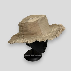May include: A beige canvas bucket hat with a frayed edge and a patchwork design. The hat is displayed on a black mannequin head.