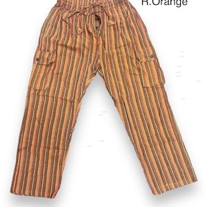 Può includere: Pantaloni a righe arancioni e marroni con vita a coulisse e due tasche laterali. I pantaloni hanno una chiusura a bottone e sono realizzati in un tessuto leggero.