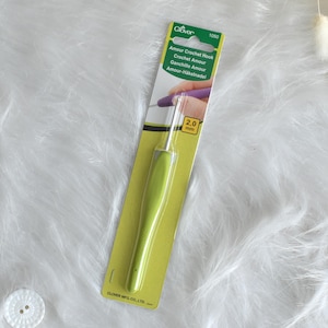 May include: A green and silver crochet hook, size 2.0 mm, on a yellow and green card. The card has the text "Amour Crochet Hook" and the Clover logo. The hook is designed for crochet projects.