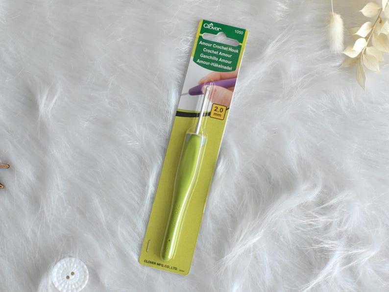 May include: A green and silver crochet hook, size 2.0 mm, on a yellow and green card. The card has the text "Amour Crochet Hook" and the Clover logo. The hook is designed for crochet projects.