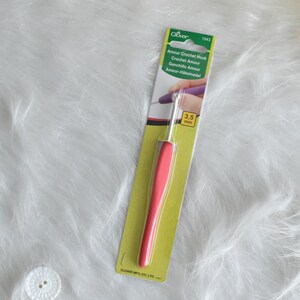 May include: A Clover Amour crochet hook with a 3.5 mm hook size. The hook has a vibrant pink handle and is packaged in a green and white card. The packaging includes the text "Amour Crochet Hook".