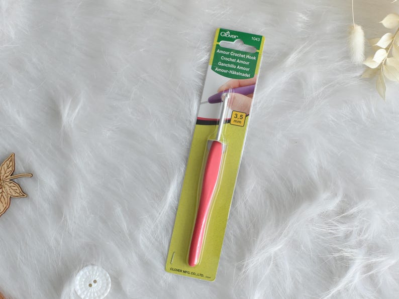 May include: A Clover Amour crochet hook with a 3.5 mm hook size. The hook has a vibrant pink handle and is packaged in a green and white card. The packaging includes the text "Amour Crochet Hook".