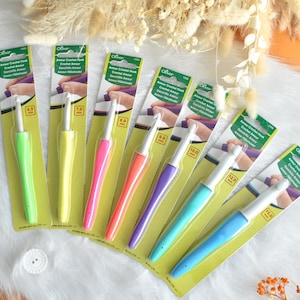 May include: A collection of Clover Amour crochet hooks in various sizes, each with a colorful, ergonomic handle. The hooks range from 6.5 mm to 15.0 mm, displayed on a white surface with decorative elements.