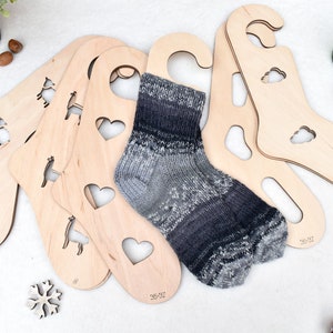 May include: Set of five wooden sock drying forms with different cutouts, including hearts, animals, and clouds. A grey and white sock is displayed on one of the forms.