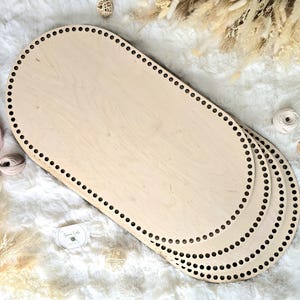 May include: Several oval wooden basket bases with pre-drilled holes for crafting. The light-coloured wood has a natural grain. The bases are surrounded by yarn and decorative elements, suggesting a crafting theme.