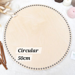 May include: A light-coloured, circular wooden base with evenly spaced holes around the perimeter. The text "Circular 50cm" is printed on the base. Crochet hooks and yarn balls in various colours are also visible.