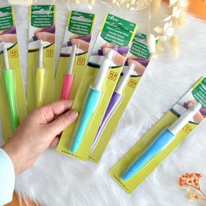 May include: A collection of Clover Amour crochet hooks in various sizes and colors, including green, yellow, pink, blue, and purple. Each hook is packaged on a yellow and green card with the hook size in millimeters.