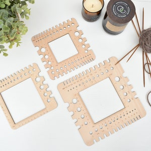 May include: Three wooden knitting stitch markers in different sizes. Each marker has a square frame with holes around the edges and a square opening in the centre. The markers are labelled with numbers in centimetres and inches.