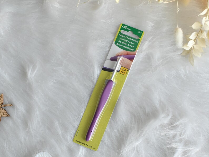 May include: A Clover Amour Crochet Hook, size 4.0 mm, with a purple handle and a silver hook. The hook is packaged on a green and yellow card with the product name and brand information.