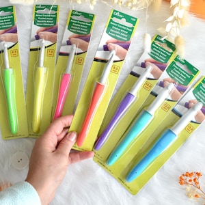 May include: A collection of Clover Amour crochet hooks in various sizes, displayed on their original packaging. The hooks have colorful handles in shades of green, yellow, pink, orange, purple, and blue. The packaging includes the hook size in millimeters.