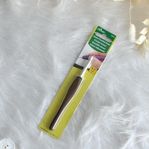 May include: A Clover Amour crochet hook, size 6.0 mm, on a yellow and green card. The hook has a brown handle and a silver metal hook. The packaging includes the text "Amour Crochet Hook" in multiple languages.