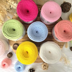 May include: A collection of colorful yarn skeins in various shades, including pink, yellow, green, and blue. The yarn is arranged on a wooden surface, with additional decorative elements like dried flowers and small wooden buttons.