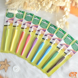 May include: A collection of Clover Amour crochet hooks in various sizes and colors, including green, yellow, red, purple, blue, and brown. Each hook is packaged in a green and white card with the hook size clearly marked.