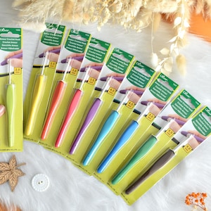 May include: A collection of Clover Amour crochet hooks in various sizes, each with a colorful, ergonomic handle. The hooks range from 2.0 mm to 6.0 mm, displayed on a white surface with decorative elements.