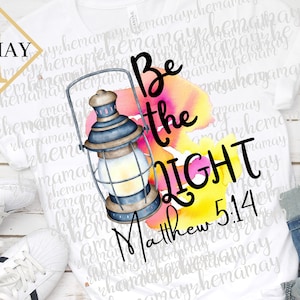 May include: White t-shirt with a watercolor design of a lantern and the words "Be the Light" with the scripture reference "Matthew 5:14".
