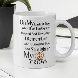 Puede incluir: Taza de cerámica blanca con una cita inspiradora en negro que dice "On My Darkest Days When I Feel Inadequate Unloved And Unworthy I Remember Whose Daughter I Am And Straighten My CROWN". La cita está centrada en la taza y presenta una corona dorada con un corazón rojo en la parte superior.