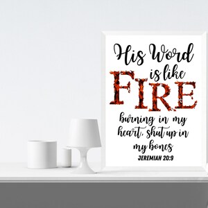 May include: A white framed print with the text "His Word is like FIRE burning in my heart, shut up in my bones JEREMIAH 20:9". The word "FIRE" is in large, bold letters and is stylized with a fiery orange and red design.