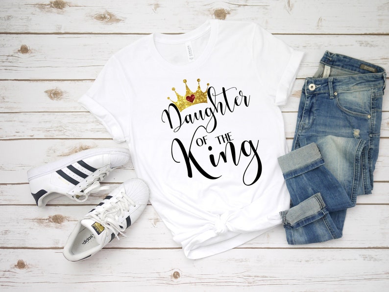 May include: White t-shirt with a gold crown and the text "Daughter of the King" in black script.