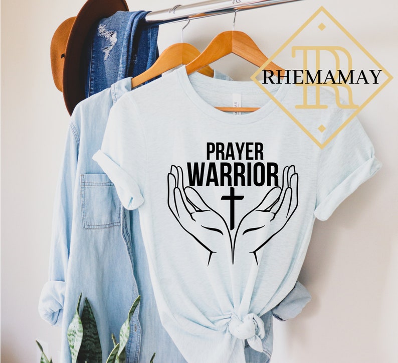 May include: A light blue t-shirt with the text "Prayer Warrior" and a cross in between two hands in a praying position.
