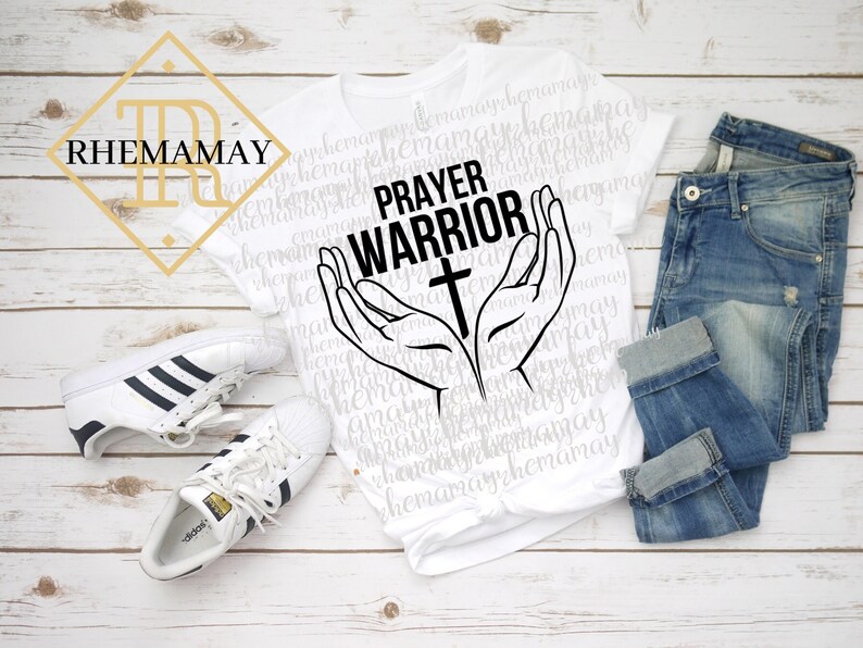 May include: White t-shirt with the text "PRAYER WARRIOR" and a cross in black. Two hands are raised in prayer with the cross in between them.
