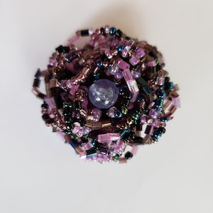 May include: A purple and black beaded flower with a purple gemstone in the center.