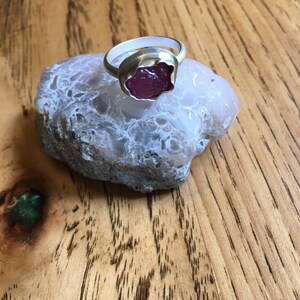 May include: A silver ring with a pink gemstone set in a flower-shaped bezel.