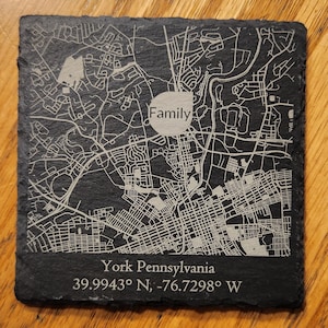 May include: Black slate coaster with a white engraved map of York, Pennsylvania. The map includes the text "Family" in a circle and the coordinates "39.9943° N, -76.7298° W".