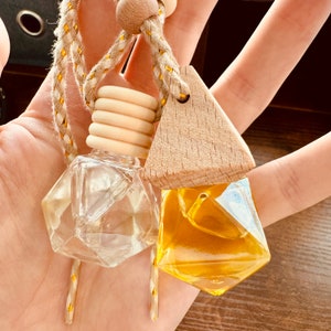 May include: Two glass car air fresheners with a geometric design, one clear and one yellow, hanging from a wooden and rope car air freshener holder.