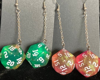 May include: A pair of dangle earrings featuring a green and pink iridescent dice charm. The dice are numbered 1-20.