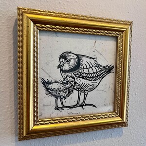 May include: A framed print showing a black and white linocut of two birds. The artwork is set within a gold-coloured frame with a textured, rope-like design. The birds are depicted with detailed linework, creating a striking contrast.