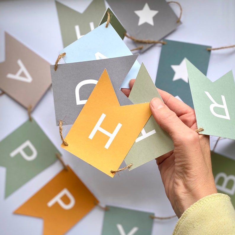 Puede incluir: Una pancarta con banderas que deletrean "Happy" en letras blancas sobre un fondo amarillo, gris y azul.