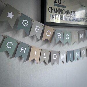 May include: A banner with the words "Georgie Childmind" in white letters on a series of green, gray, and beige triangular flags.