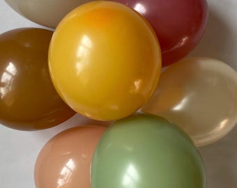 Puede incluir: Un conjunto de globos coloridos en tonos de amarillo, marrón, rosa, verde y blanco. Los globos están dispuestos muy juntos, creando una exhibición vibrante y festiva. Los globos tienen un acabado brillante.