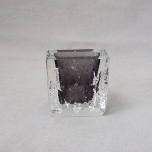 Könnte beinhalten: Eine kleine, klare Glasvase mit einer strukturierten Oberfläche und einem dunkelgrauen Innenraum. Die Vase ist quadratisch und hat einen leicht abgerundeten Boden.