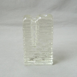 Può includere: Un vaso di vetro trasparente e rettangolare con un design strutturato a forma di corteccia. Il vaso ha due aperture nella parte superiore ed è adatto per esporre piccoli fiori o steli decorativi. Il vaso è alto circa 10 cm.