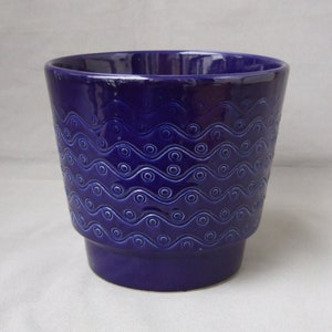 Op de afbeelding: Een diepblauwe keramische plantenpot met een golvend patroon. De pot heeft een brede basis en een licht uitlopende bovenkant.