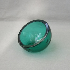 May include: A teal green glass bowl with a rounded shape. The bowl has a smooth, glossy finish.