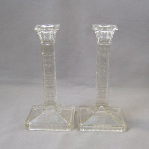 Può includere: Un paio di portacandele in vetro trasparente con base quadrata e design testurizzato. I portacandele sono alti e sottili.