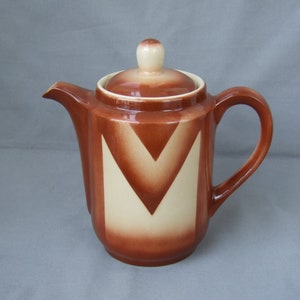 Op de afbeelding: Een bruine koffiekan van keramiek met een wit geometrisch ontwerp. De kan heeft een deksel en een handvat.