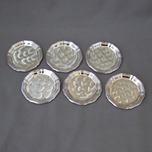 Può includere: Sei sottobicchieri color argento con un design decorativo in rilievo. I sottobicchieri sono rotondi e hanno un bordo smerlato.
