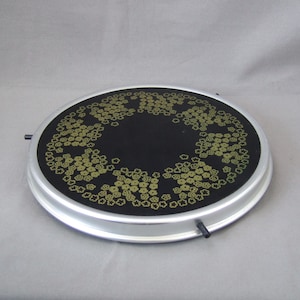 Puede incluir: Una bandeja redonda para servir de color plateado con un centro negro y un patrón decorativo de flores doradas alrededor del borde.